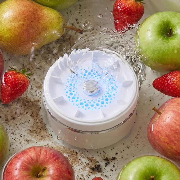 Das eingeschaltete Gerät PuriEasy am Boden eines mit Wasser gefüllten Gefäßes, umgeben von Äpfeln und Erdbeeren